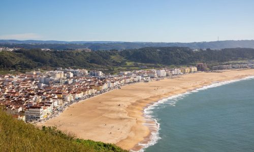 A picturesque beach landscape featuring a wide expanse of sand and a line of houses on the hill in the background